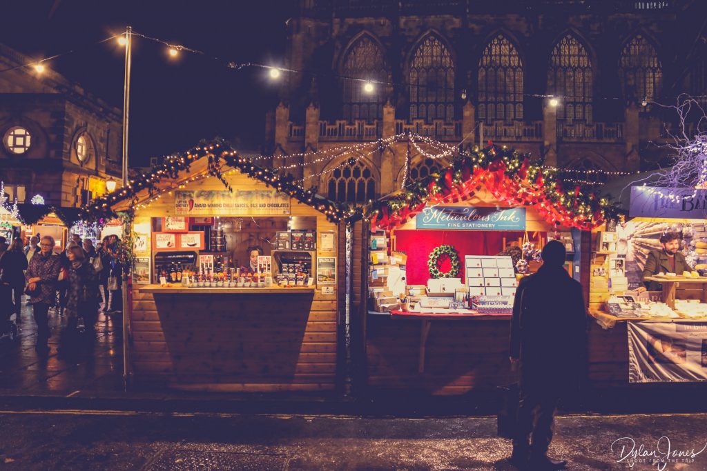Bath Christmas Market stall holders selling chilli based products and stationery with the backdrop of Bath Abbey