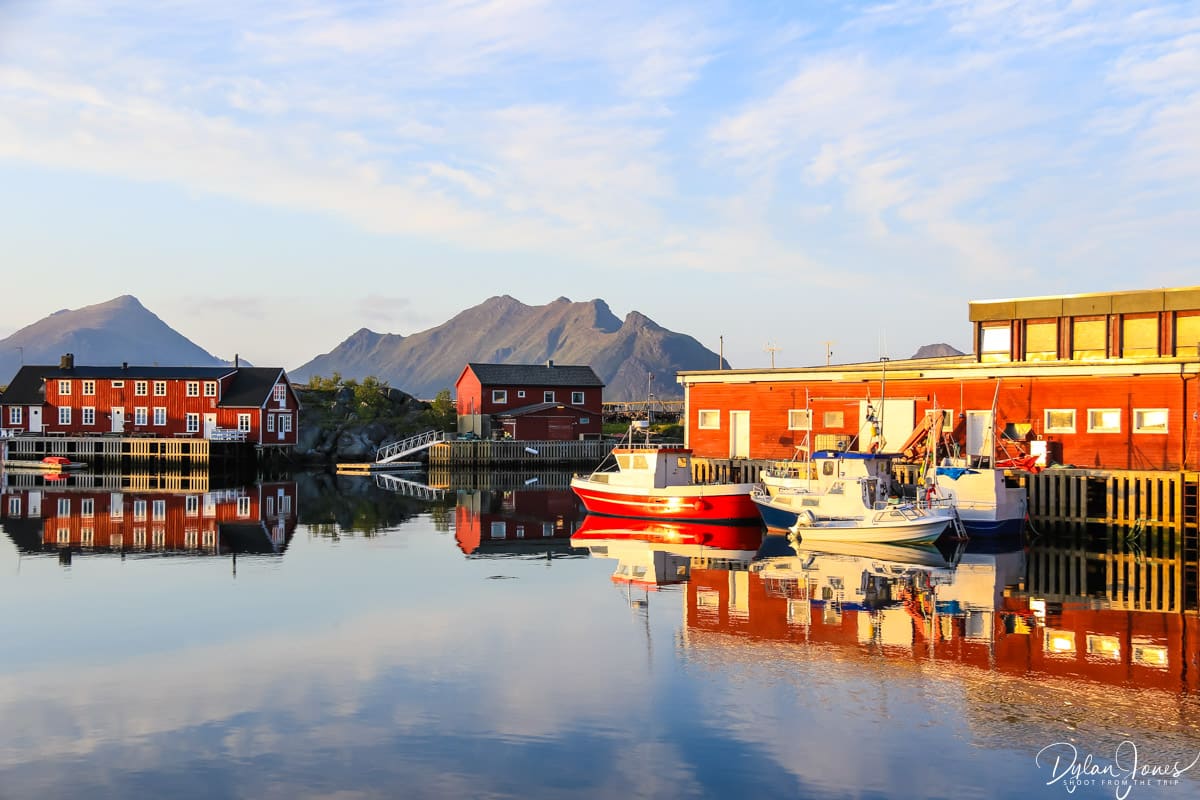Views across Ballstad harbour of red wooden buildings with a mountain backdrop